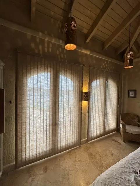 Light-filtering shades on arched French doors in a bedroom with a beamed wood ceiling