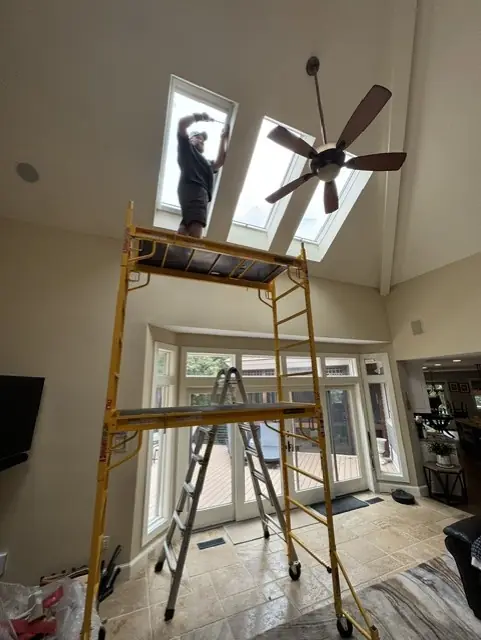 Installer on scaffolding fitting shades to skylights in a cathedral ceiling