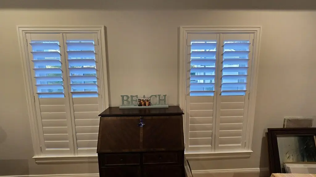 White plantation shutters on two windows flanking an antique secretary desk