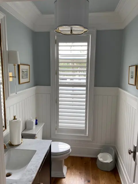 Tall plantation shutter in a powder room with white wainscoting